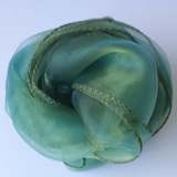 A rolled piece of sheer green organza fabric with olive green braided trim, photographed on a plain light background.