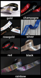 A collage showing multiple satin ribbon color options labeled gold, champagne, rosegold, silver, red, black, and rainbow. Each panel shows the ribbon curled and laid out with printed text, on a dark or wood background.