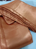 A folded piece of shiny copper-brown satin ribbon or trim with stitched edges, placed on a light blue fabric surface.