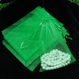 Green sheer organza drawstring pouches, one filled with white faux pearls, displayed on a black velvet background.