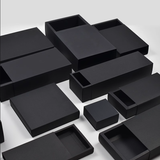 A set of black sleeve drawer gift boxes, arranged on a light gray studio background.