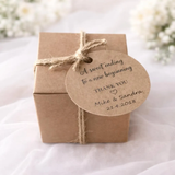 A small square kraft paper gift box tied with natural jute twine and a round kraft paper tag that reads 'A sweet ending to a new beginning THANK YOU Mike & Sandra 21.4.