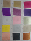 A grid of small fabric or material swatches in many colors, including beige, gold, pink, purple, white, silver, yellow, peach, black, and orange, arranged on a printed chart with numbered labels.